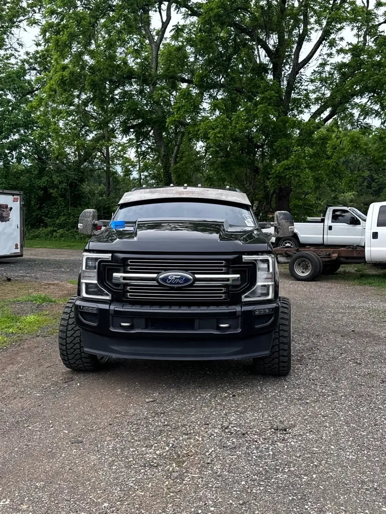 Front view of black Ford pickup truck with wide tires parked outdoors on gravel