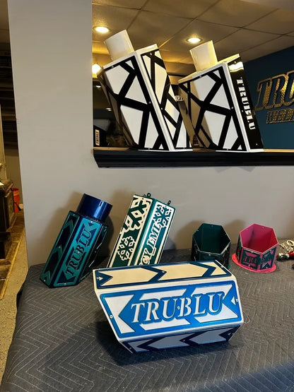 Custom metal fabricated parts with geometric patterns and TRU BLU logo on display indoors