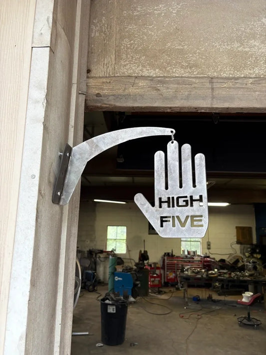 Metal high five hand sign mounted by a workshop door, industrial shop in background