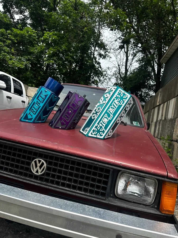 Colorful custom metal boxes with geometric designs displayed on a red Volkswagen car hood outdoors