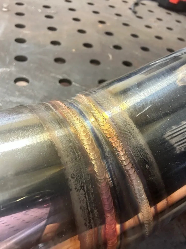 Close-up of stainless steel pipe with colorful TIG weld bead on metal workbench