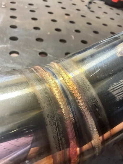 Close-up of stainless steel pipe with colorful TIG weld bead on metal workbench