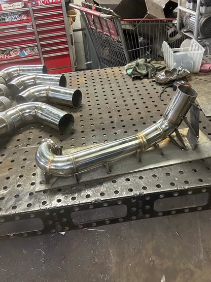 Custom stainless steel exhaust pipe on metal workbench in automotive fabrication shop