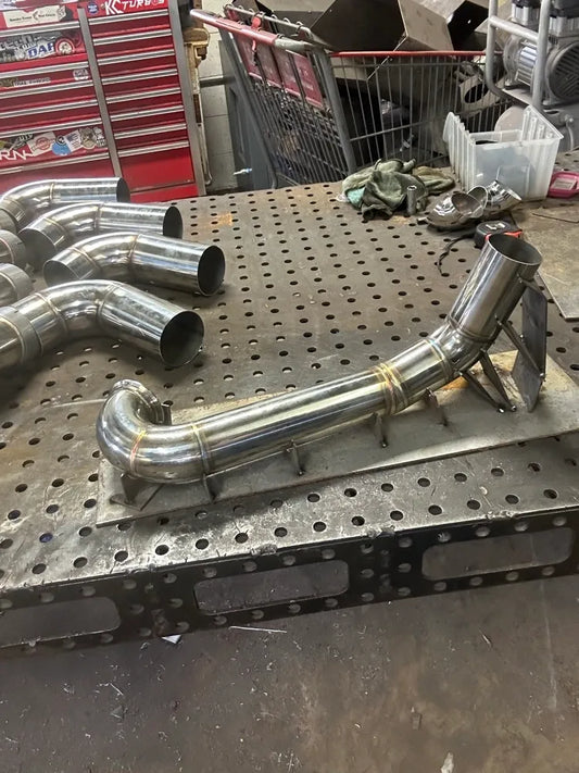 Custom stainless steel exhaust pipe on metal workbench in automotive fabrication shop