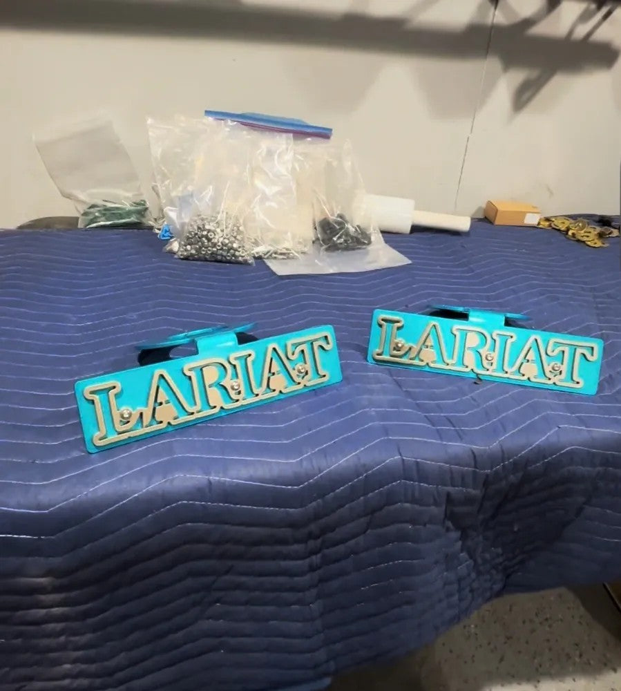 Two turquoise LARIAT truck emblems on a blue quilted surface, workshop background