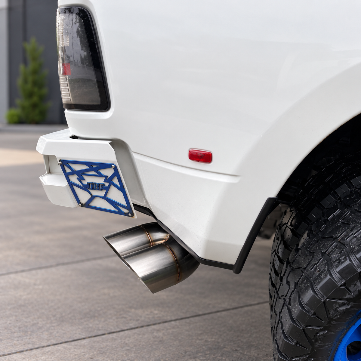 Stainless steel dual mitre exhaust tip installed below the rear corner of a white truck